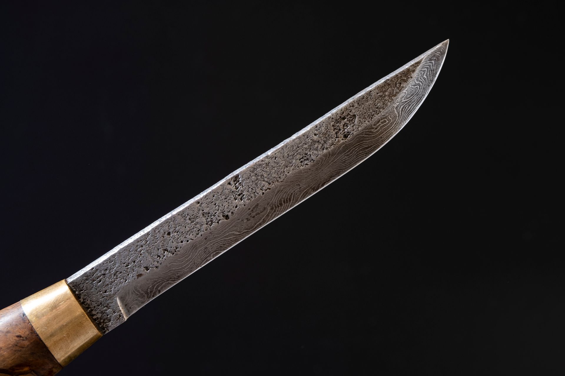 Macro close-up of layered damascus steel patterning on a knife blade against a black background